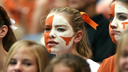 Blonde woman with orange and white face paint watching a football match