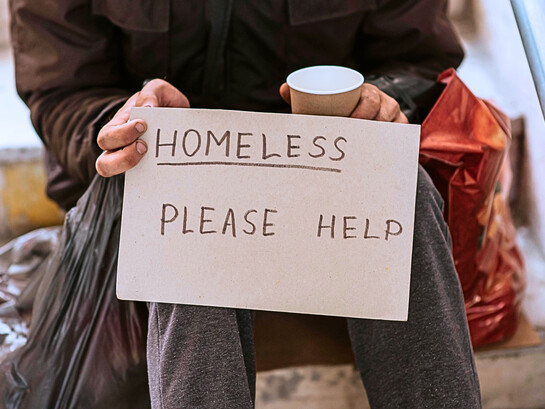 A person holding a sign stating homelessness, representing the failure of institutions to ensure safe and dignified housing