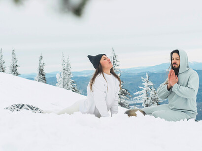 A couple finding balance in the snow, embodying yoga’s ability to stabilise body and mind in winter