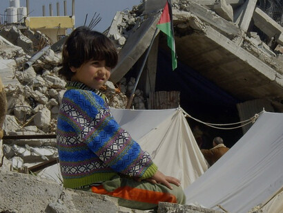 In the southern Gaza Strip, a child sits before a destroyed home, amid hunger and devastation