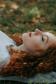 A moment of tranquility: a young woman with vibrant red hair rests on a soft blanket amidst the lush green grass