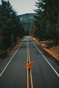 A person balancing their arms while walking through the middle of a forest road