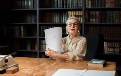Une femme âgée montrant un livret alors qu'elle est assise dans une bibliothèque