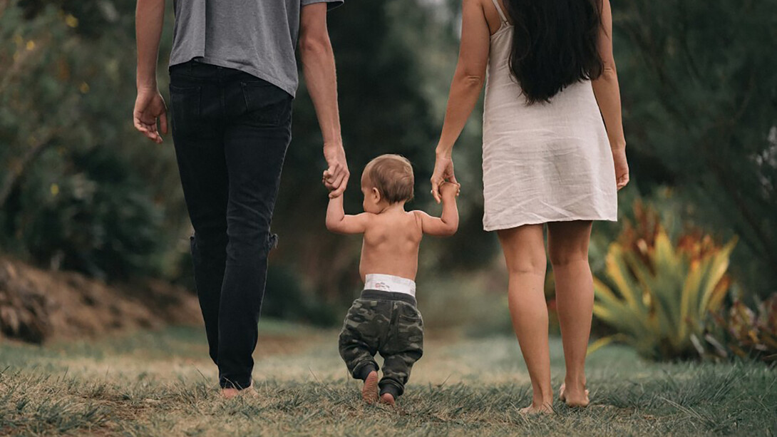 A couple walks barefoot through the garden, holding hands with their child