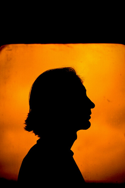 Silhouette of a person in a dark room before a window glowing with red and yellow light