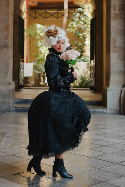 A woman in a luxurious Baroque-inspired gown stands before a grand neoclassical building