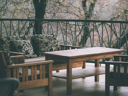 Una terrazza accogliente immersa nella natura autunnale, con sedute in legno e cuscini decorativi. Gli alberi spogli sullo sfondo trasmettono quiete e introspezione