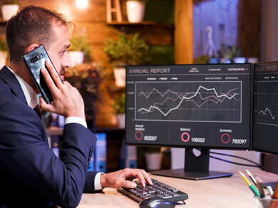 The manager speaks on the phone while analyzing financial graphs and stock market trends on the monitor, refining trading strategies for options trading