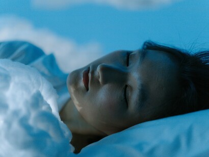 A woman sleeping with glowing cloud shapes around her, reminding us that sleep fuels recovery and focus