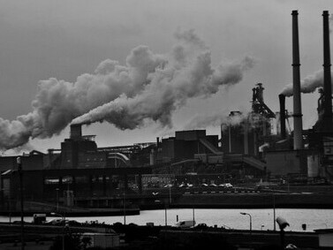 Grayscale photograph of smokestacks releasing heavy carbon emissions, symbolizing fossil fuel pollution and the consequences of burning coal and oil, Rotterdam, ZH, Netherlands