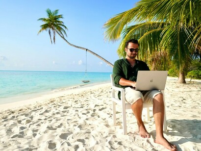 A man sitting on a chair on a beach, working on his laptop as a freelancer in the Maldives