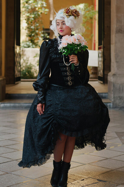 A woman wearing an elegant Baroque-inspired costume stands in front of a classical building