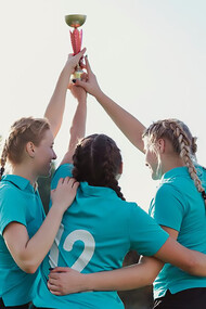Girls celebrating with raised trophies at an awards ceremony, showcasing community recognition and public appreciation events