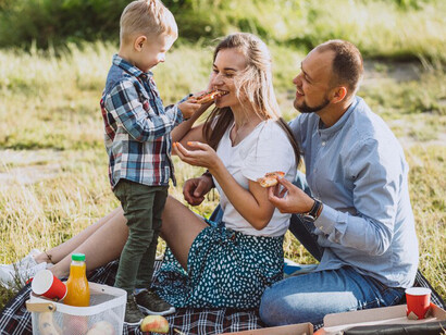 A family gathers in the park for a picnic, savoring slices of pizza under the open sky