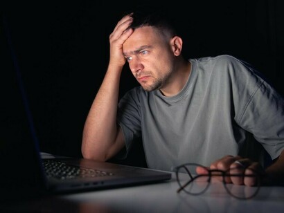 An upset young man working alone at his computer late at night
