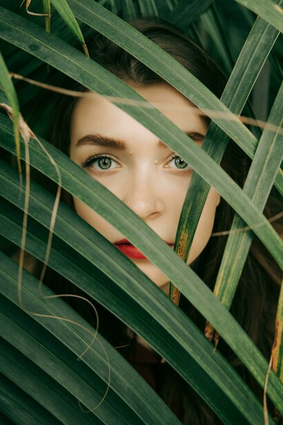 A woman’s face emerging from behind green leaves, evoking themes of self-discovery and authentic meaning