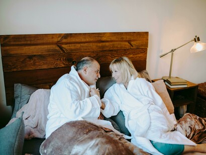 A happy older couple relaxing in bed, wrapped in white robes and kissing affectionately