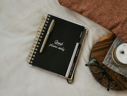 On a quiet bed rests a notebook with a pen, its cover carrying the message 'Good Pplans only'