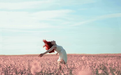 A woman in a yellow dress stands in a field covered with pink petals