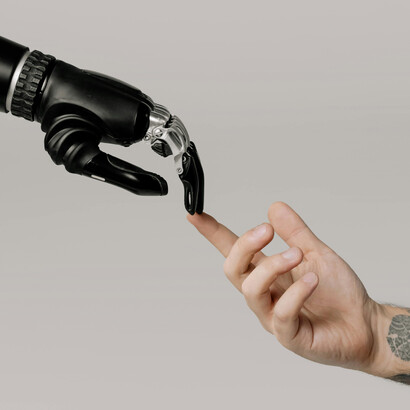 A human and robotic hand meet, representing the intersection of technology and humanity