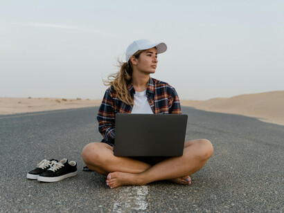 A woman sits by a desert road with her laptop, blending work and travel in a nomadic lifestyle