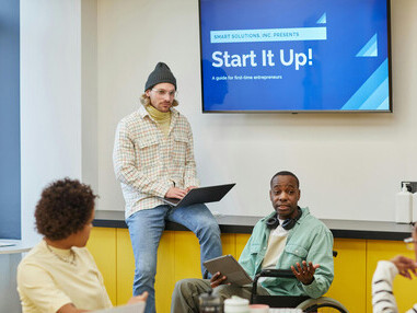 A man presents in front of his startup team in a meeting room, guiding a brainstorming session where founders and colleagues collaborate on their business pitch