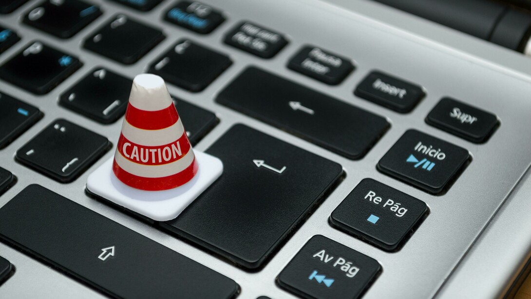 White caution cone placed on a computer keyboard symbolizing warnings about data privacy, ethical risks, and inequality in the digital world