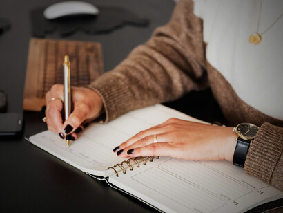 A woman carefully writes in her diary, her pen poised with focus and reflection