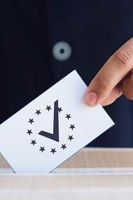 A close-up of a man casting his vote, placing a ballot into the ballot box