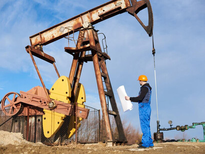 The pump jack in operation and engineers working on the oil field under a clear, sunny sky