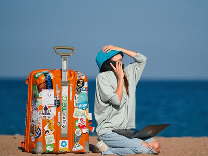 A woman standing on a beach with a suitcase, embracing the freedom of a nomadic lifestyle and working from anywhere