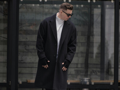 A fashionable man wearing a black coat and sneakers walking outdoors