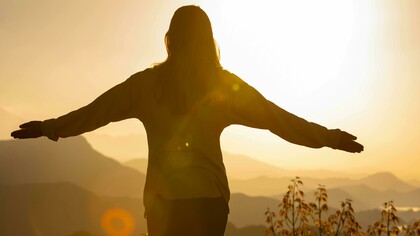 Una persona che apre le braccia al tramonto come forma di meditazione e gratitudine