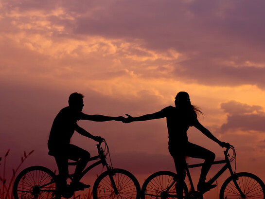 A woman on a bike reaching out to take the hand of a man riding behind her, both enjoying a moment of connection