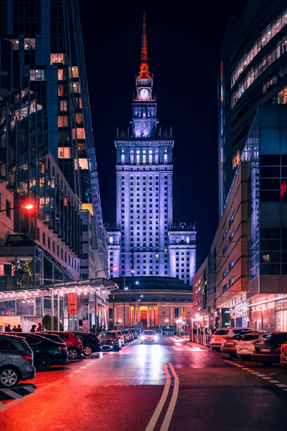 Warsaw's skyline at night, featuring a brightly lit Ferris wheel in the background, with bustling city roads and a lively urban ambiance