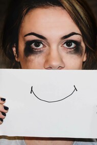 Communicating the false sense of happiness by drawing a smile on a piece of paper and hanging it in front of the mouth to mask the misery
