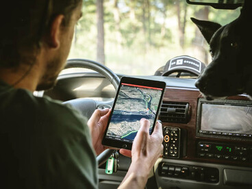 A man in a gray shirt is holding a black tablet displaying the car's GPS navigation system
