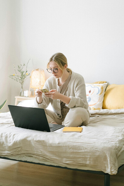 Woman working on a black laptop while seated on her bed