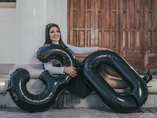 A woman sitting on the floor with balloons, celebrating her 30th birthday