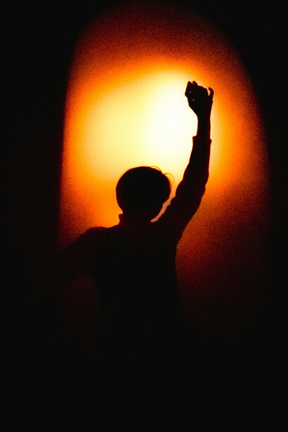 Person’s silhouette inside a dim room, framed by a window lit with red and yellow tones