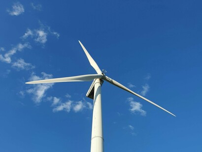 The clean lines of a wind turbine contrast with the natural beauty of a blue sky and white clouds, symbolizing the integration of technology and nature in renewable energy solutions