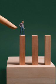 One individual is seen attempting to make the dominoes fall, symbolizing the pressure placed on employees to meet unrealistic expectations 