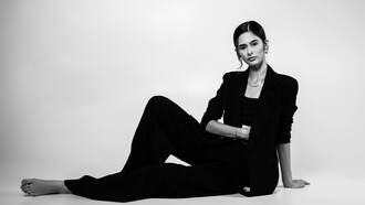 A portrait of a female model posing confidently in a studio, dressed in a sleek black suit that embodies modern sophistication and timeless style