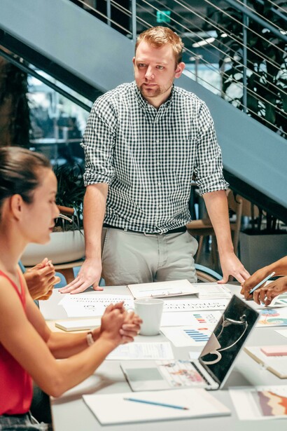 A man in a black and white checkered shirt sits next to a woman in an orange tank top during a startup meeting