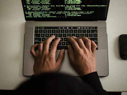 An unrecognizable developer working on a laptop and smartphone beside a custom PC built with high-end computer hardware