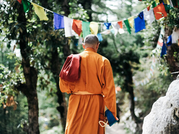 An unidentifiable Buddhist monk meditating quietly in a serene garden filled with greenery and flowers in Nepal, symbolizing peace and mindfulness