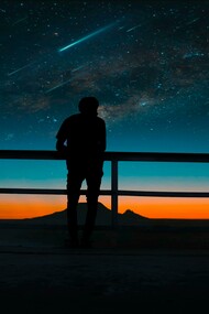 Under the night sky, a person gazes at shooting stars and meteors