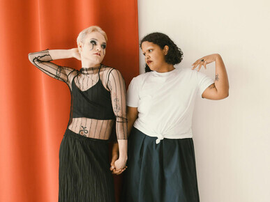 A woman in a black dress leaning on a woman in a white shirt, a lesbian couple