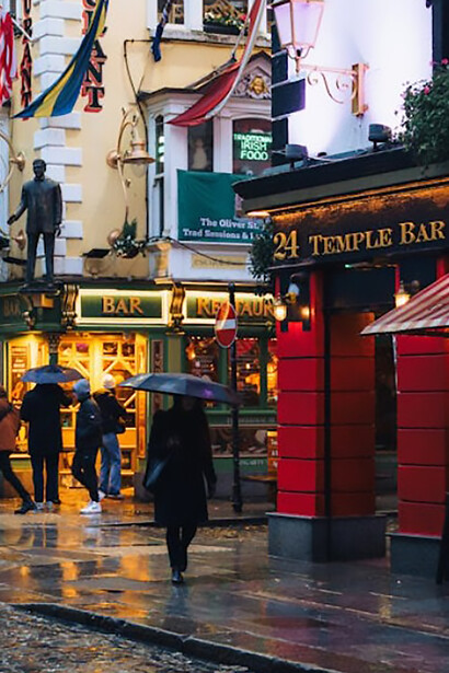 People with umbrellas walking in the rain beneath festive Christmas lights in Temple Bar, Dublin, Ireland