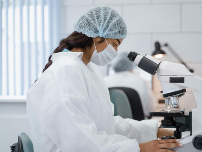 A woman wearing a face mask looks through a microscope while working in an AI-powered laboratory